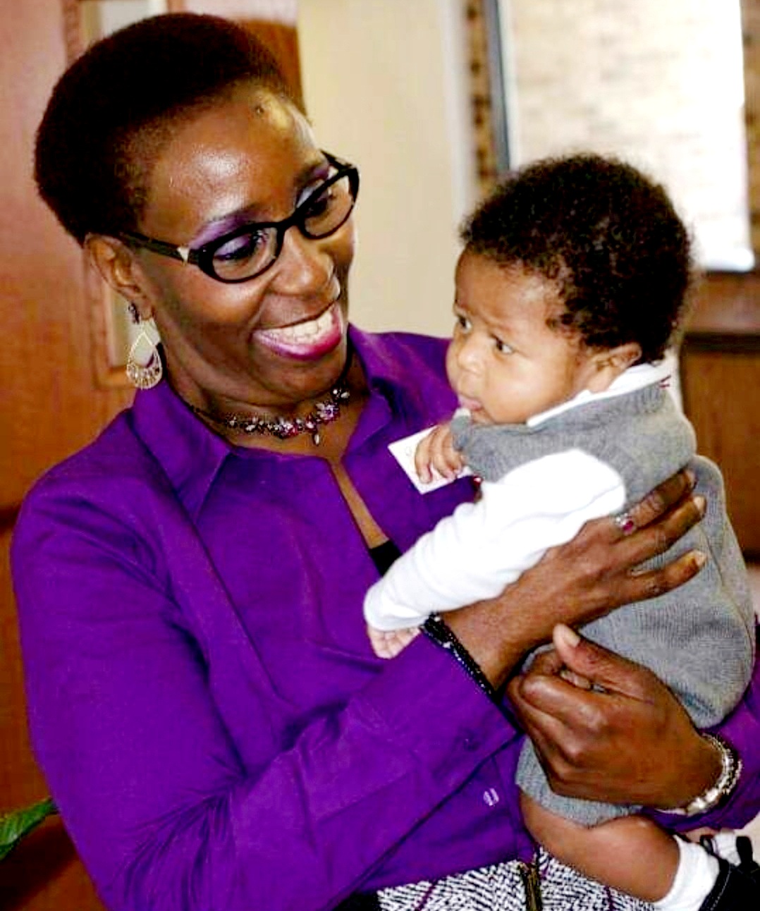 an African American grandma in a purple dress holding her infant grandson