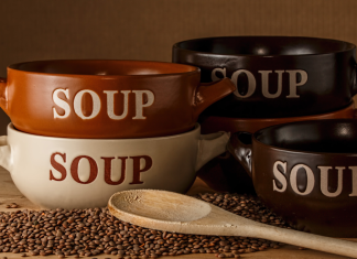 a stack of bowls with the word, "soup" printed on the front, next to a wooden spoon and some lentils spilled out on a counter