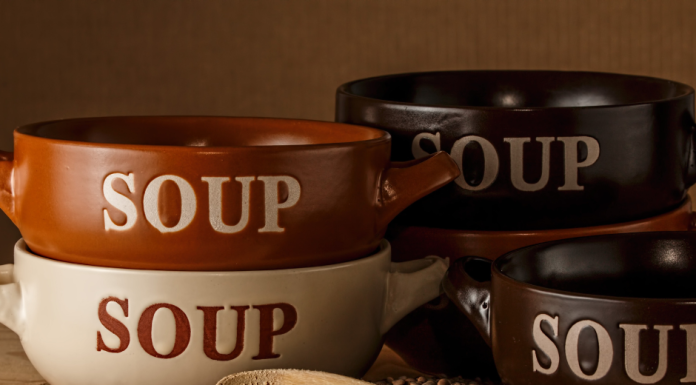 a stack of bowls with the word, "soup" printed on the front, next to a wooden spoon and some lentils spilled out on a counter