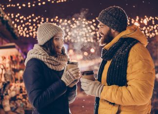 a couple drinking coffee outside by Christmas lights on a date night