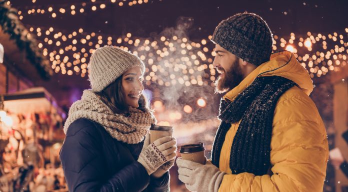 a couple drinking coffee outside by Christmas lights on a date night