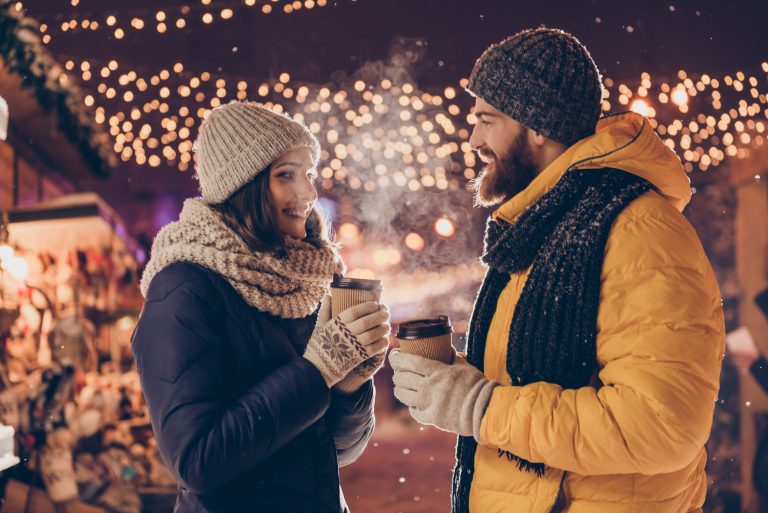 a couple drinking coffee outside by Christmas lights on a date night