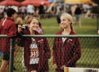 two tween girls in track uniforms standing by a chain link fence