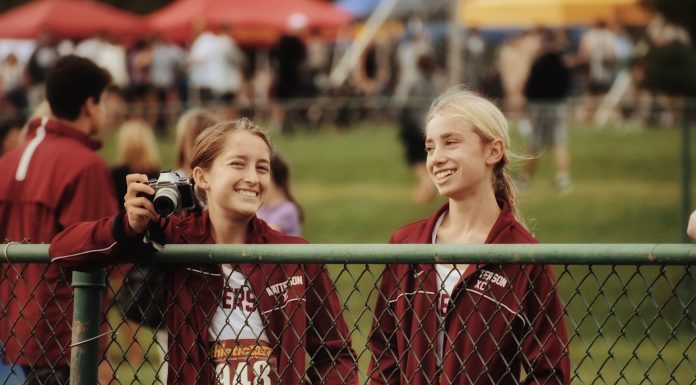 two tween girls in track uniforms standing by a chain link fence