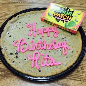 a box of Sour Patch Kids resting on a cookie cake that says, “Happy Birthday, Rita” in pink icing