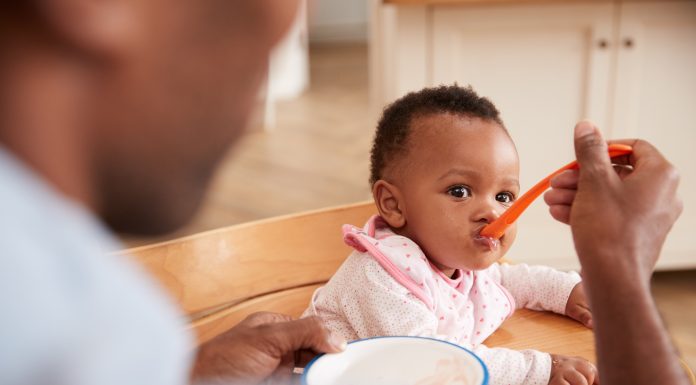 An African-American father spoon-feeding a baby in a highchair