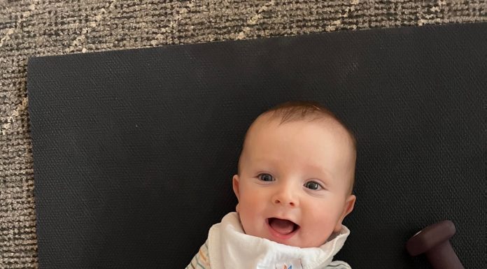 a baby laying on a mat, smiling up at his mon