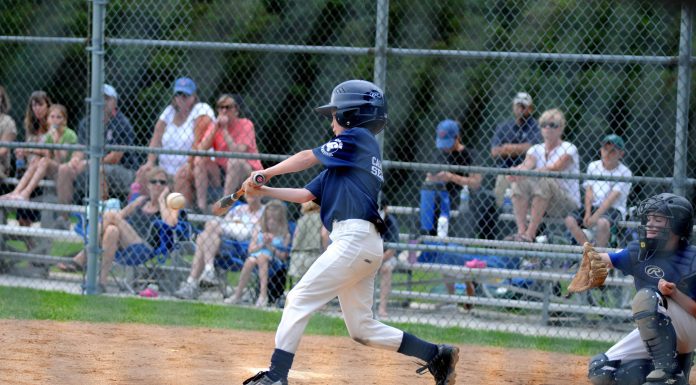 a boy hitting a baseball as parents and fans look on with sportsmanship