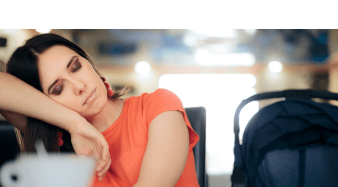 a sleepy mom with her head leaning on her arm, eyes closed, with a mug of coffee in front of her on the table