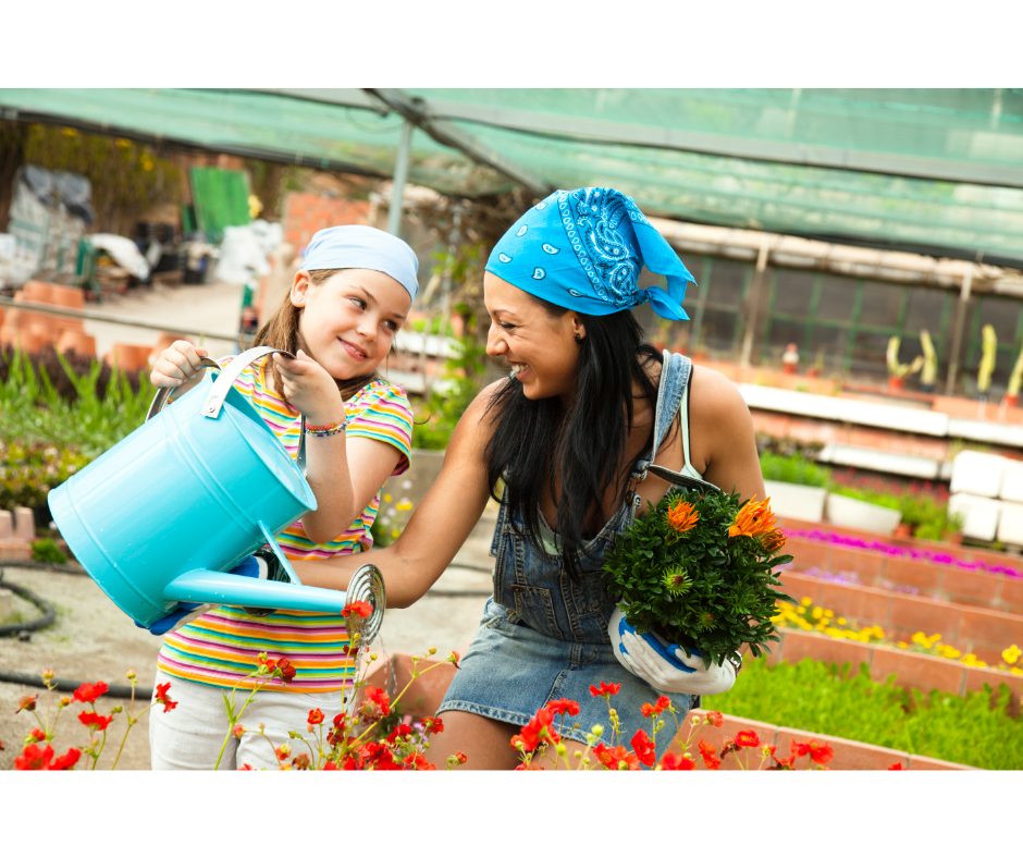 a mom with her daughter in the garden, both wearing bandanas on their heads, as the daughter pours from a watering can
