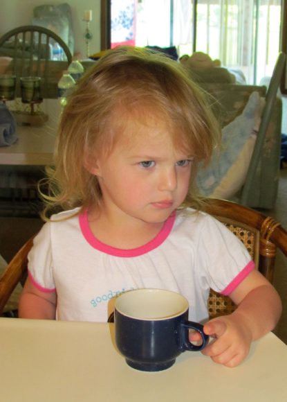 a girl sitting at counter, frowning as she holds a coffee mug