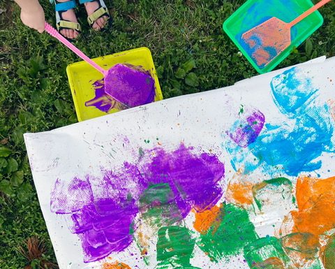 children painting on large sheets of paper outside in the grass as part of their art-making