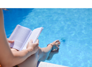 a photo from above of a woman sitting with her feet in the pool as she reads a book