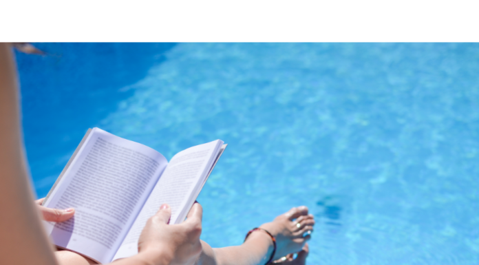 a photo from above of a woman sitting with her feet in the pool as she reads a book