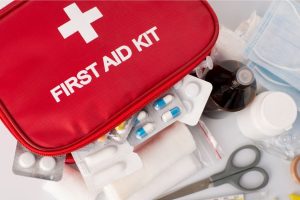 A red first aid kit that has first aid supplies scattered around it