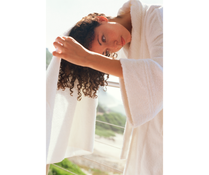 a woman with curly hair in a bathrobe on a balcony, wrapping a towel around her hair