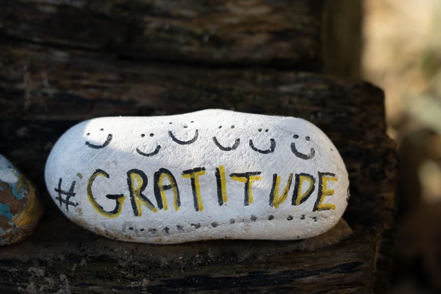 a rock painted white with smiley faces and the word Gratitude on it