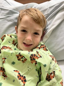 a boy in a hospital gown laying in a hospital bed. prior. to having a Tonsillectomy