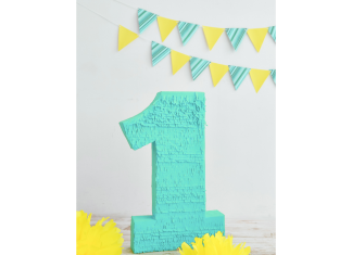 a turquoise pirata shaped like a one on a table with yellow tissue paper flowers and a turquoise and yellow flag banner in the background to symbolize a first birthday