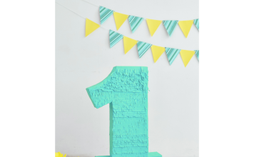 a turquoise pirata shaped like a one on a table with yellow tissue paper flowers and a turquoise and yellow flag banner in the background to symbolize a first birthday