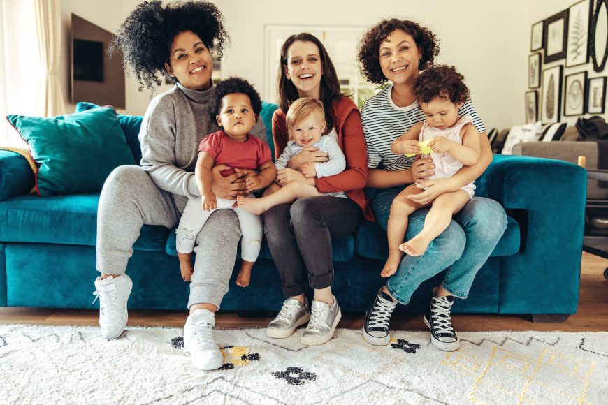 single mom support Multi-ethnic mommies sitting with children. Young mothers with babies sitting on sofa and looking at camera.