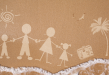 a stick figure family drawing in the sand with ocean water lapping up at the bottom of the photo, displaying a family vacation