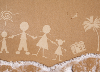 a stick figure family drawing in the sand with ocean water lapping up at the bottom of the photo, displaying a family vacation