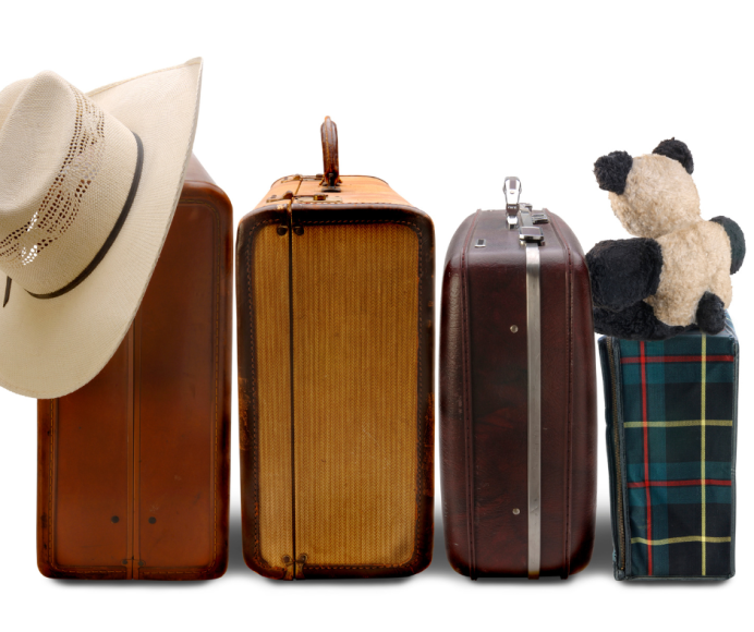 four suitcases, side by side, one of which has a cowboy hat resting on it and another with a teddy bear on it, symbolizing a family vacation