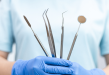 a close up of a dentist holding tools, wearing rubber gloves