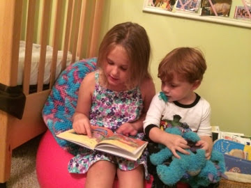 a young girl sitting on a bean bag chair with her baby brother, reading him books