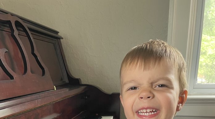 a young boy smiling as he plays the piano during music lessons