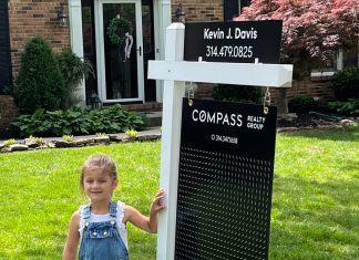 as moving day approaches, a young girl stands next to a for sale sign in her yard