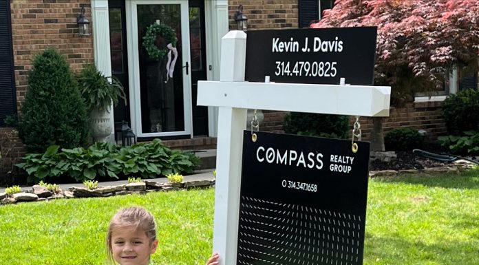 as moving day approaches, a young girl stands next to a for sale sign in her yard