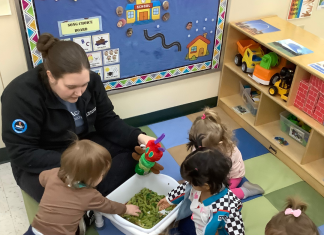 a group of preschool children sitting on a carpet with their Kiddie Academy teacher