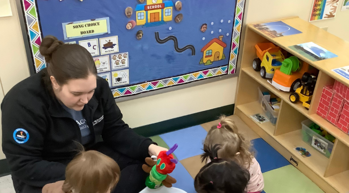 a group of preschool children sitting on a carpet with their Kiddie Academy teacher