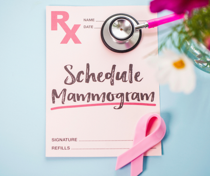 a prescription on pink paper that says, Schedule Mammogram. A pink stethoscope and a pink ribbon sit nearby along with flowers.