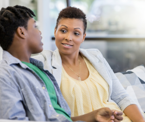 a mom sitting on the couch, talking to her teenaged son, checking in on the mental health needs of her children