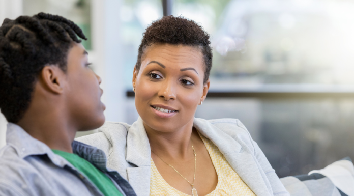 a mom sitting on the couch, talking to her teenaged son, checking in on the mental health needs of her children