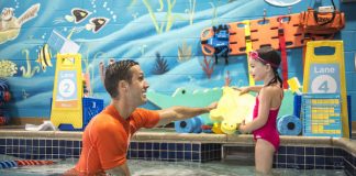 a male swim instructor encouraging a young girl to swim at Goldfish Swim School