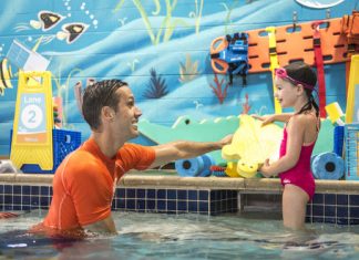 a male swim instructor encouraging a young girl to swim at Goldfish Swim School