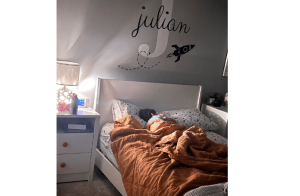 little boy asleep in his bed with a nightlight one. the name julian on his wall. orange blanket.