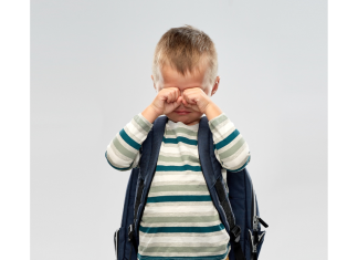 a young boy wearing a backpack, wiping tears from his eyes as he has a meltdown after school