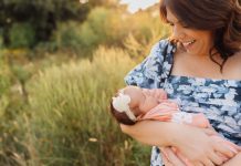 a mom gazing at the newborn baby in her arms as she stands out in a field