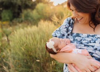 a mom gazing at the newborn baby in her arms as she stands out in a field