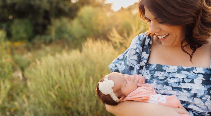 a mom gazing at the newborn baby in her arms as she stands out in a field