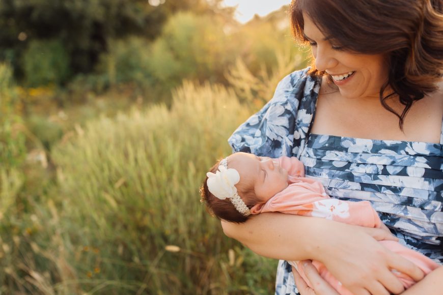 a mom gazing at the newborn baby in her arms as she stands out in a field