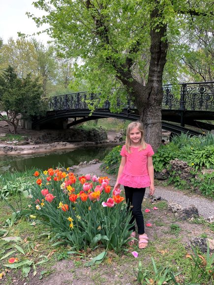 a girl standing by a bridge and spring flowers