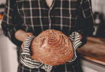 a woman wearing oven mitts as she holds a loaf of sourdough