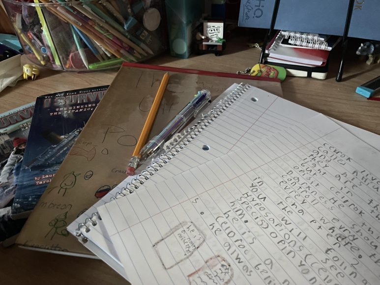 A young authors desk set up with a notebook, a story in progress, a printed book and copies of his favorite Lauren Tarshis books.