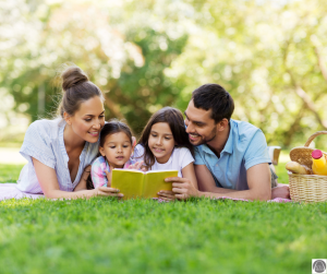 a mom and dad with their two young kids laying in the grass as they build community by reading a book together